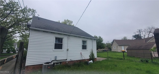 view of side of home with a yard, fence, a shingled roof, and cooling unit