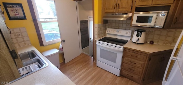 kitchen with light wood-style flooring, under cabinet range hood, white appliances, light countertops, and tasteful backsplash