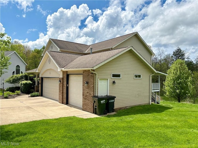 view of side of property with a garage, a lawn, driveway, brick siding, and roof with shingles