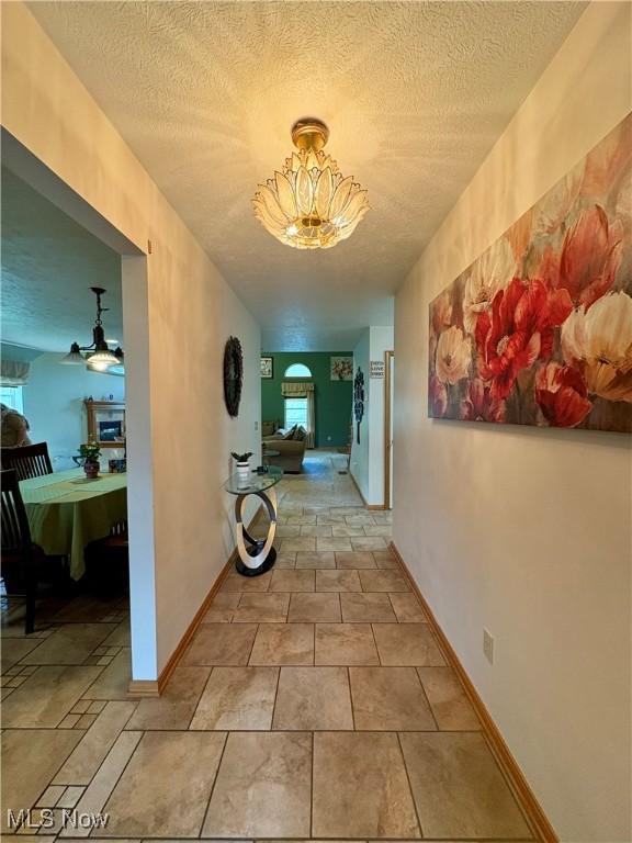 hallway featuring a textured ceiling, a notable chandelier, and plenty of natural light