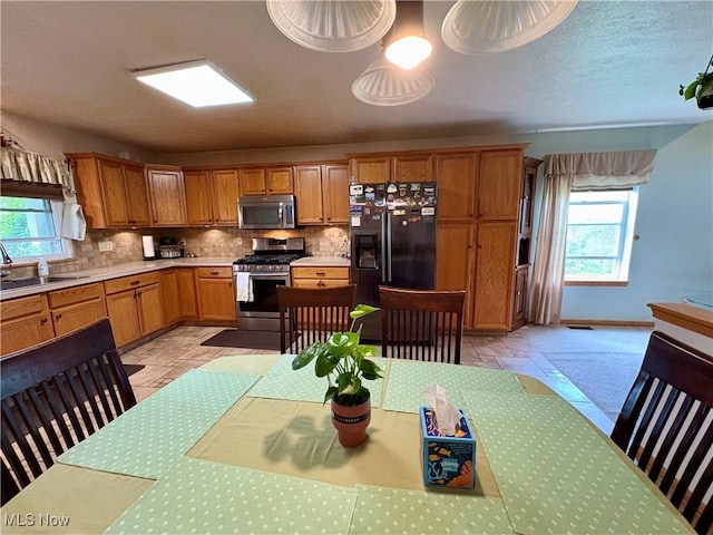 kitchen with stainless steel appliances, brown cabinetry, a sink, backsplash, and light countertops