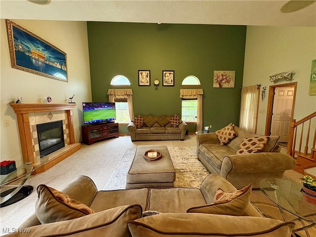 living area with carpet flooring, a tile fireplace, a high ceiling, and stairway