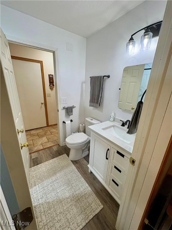 half bath featuring toilet, wood finished floors, and vanity