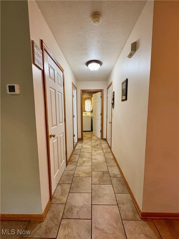 hall featuring a textured ceiling, baseboards, and light tile patterned floors