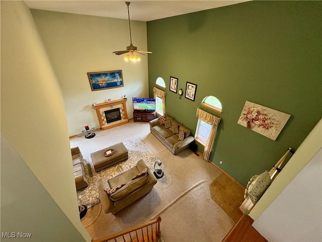 living room with ceiling fan, carpet flooring, high vaulted ceiling, and a glass covered fireplace