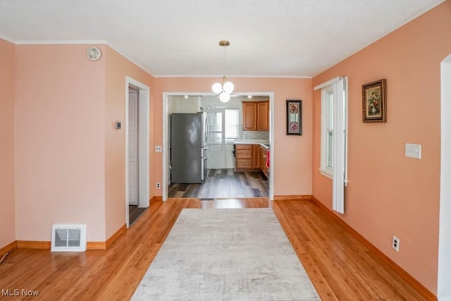 interior space with light wood-type flooring, baseboards, ornamental molding, and visible vents