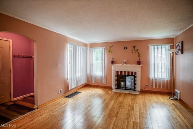 unfurnished living room with arched walkways, a wealth of natural light, hardwood / wood-style floors, and a brick fireplace
