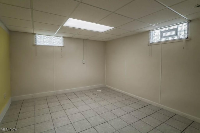 basement featuring a paneled ceiling, baseboards, light tile patterned floors, and plenty of natural light