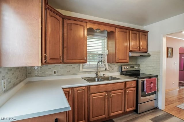 kitchen featuring a sink, under cabinet range hood, backsplash, light countertops, and electric range