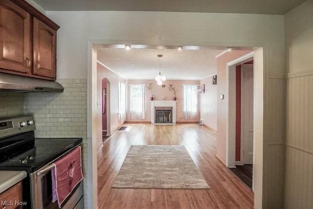 kitchen featuring stainless steel range with electric stovetop, light wood finished floors, a fireplace, and under cabinet range hood