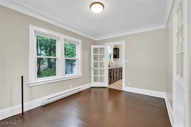 empty room with baseboards, dark wood-style flooring, baseboard heating, and a sink