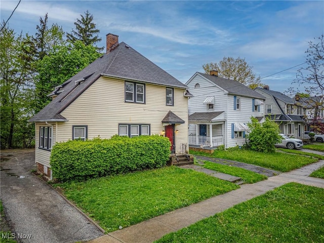 view of front of property featuring a shingled roof, a chimney, and a front yard
