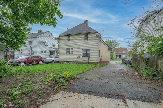 rear view of house with fence, driveway, and a chimney