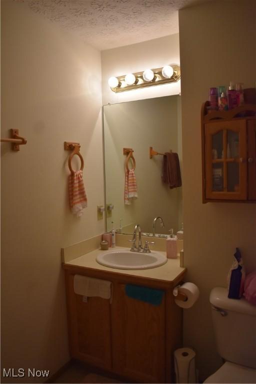 half bathroom featuring a textured ceiling, toilet, and vanity