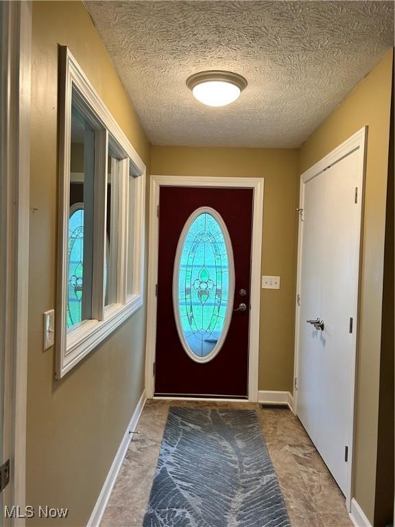 doorway to outside with baseboards and a textured ceiling