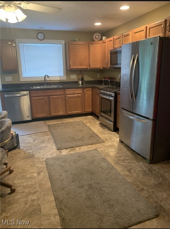 kitchen featuring a sink, stainless steel appliances, brown cabinets, a ceiling fan, and dark countertops