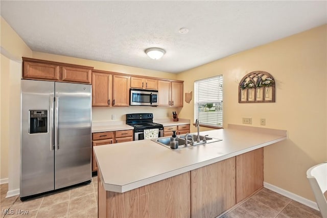 kitchen with light tile patterned floors, baseboards, a sink, a peninsula, and stainless steel appliances