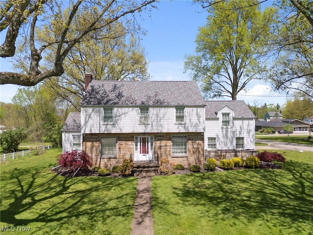 view of front facade featuring stone siding, fence, a chimney, and a front yard