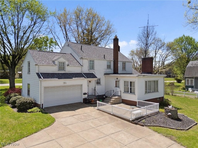 view of front facade featuring a chimney, driveway, an attached garage, a shingled roof, and a front yard