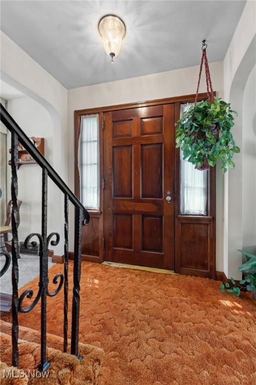 entryway with light colored carpet, stairs, and arched walkways