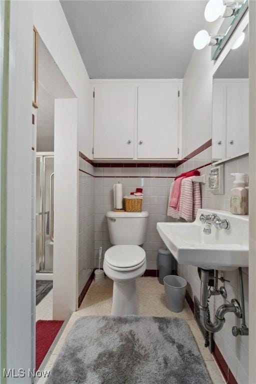 bathroom featuring tile patterned floors, tile walls, toilet, and a shower stall
