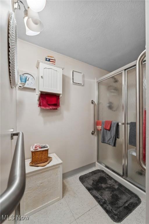bathroom featuring a stall shower, a textured ceiling, and baseboards