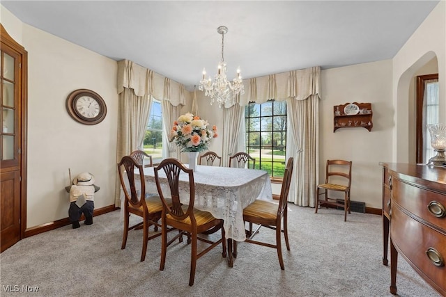 dining room featuring a chandelier, baseboards, arched walkways, and light carpet