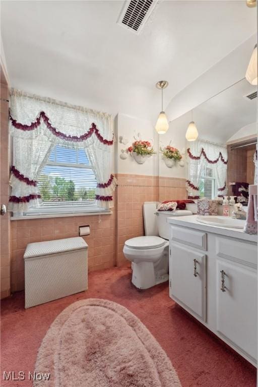bathroom with toilet, tile walls, visible vents, wainscoting, and vanity