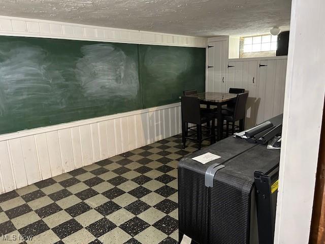 interior space with a textured ceiling, a wainscoted wall, and tile patterned floors