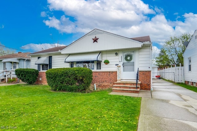 bungalow-style home featuring fence, brick siding, concrete driveway, entry steps, and a front lawn