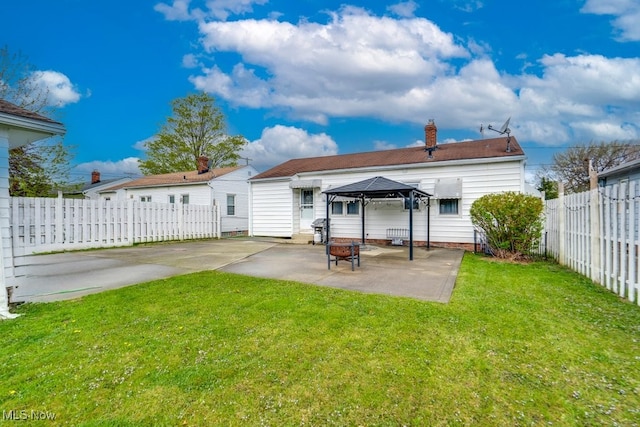 rear view of property featuring a gazebo, a patio, a fenced backyard, a chimney, and a lawn