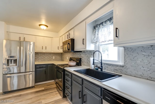 kitchen with a sink, light wood-type flooring, black appliances, light countertops, and tasteful backsplash