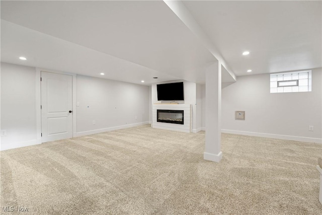 below grade area featuring recessed lighting, light carpet, baseboards, and a glass covered fireplace