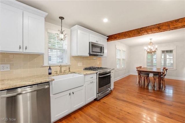 kitchen with light wood finished floors, appliances with stainless steel finishes, a chandelier, and baseboards