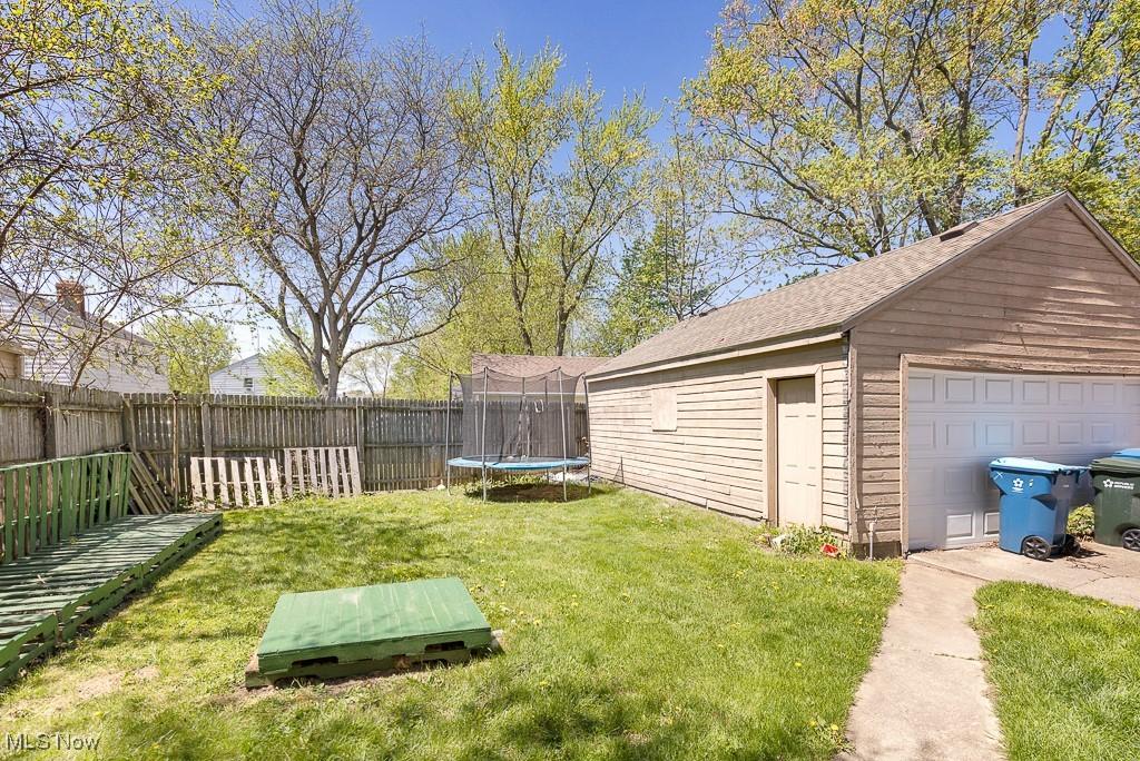 view of yard with a trampoline, an outdoor structure, a fenced backyard, and a detached garage