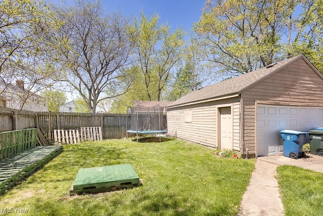 view of yard with a trampoline, an outdoor structure, a fenced backyard, and a detached garage