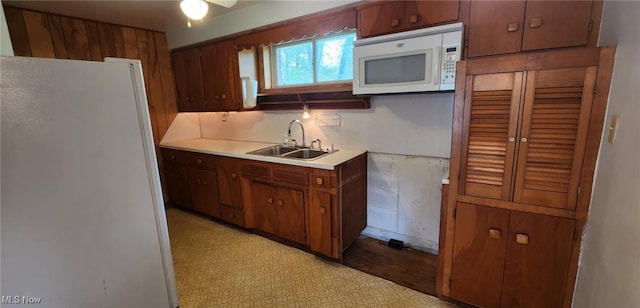 kitchen with light floors, white appliances, a sink, brown cabinets, and light countertops