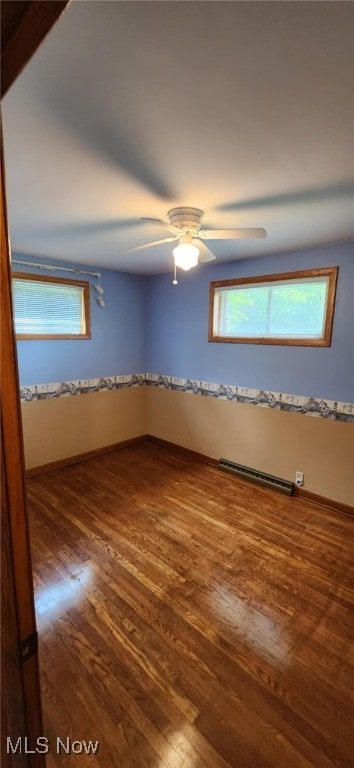 spare room featuring a wealth of natural light, baseboard heating, and wood finished floors