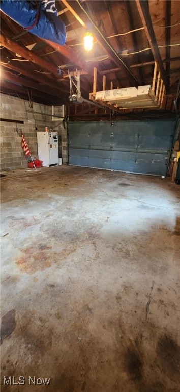 garage with freestanding refrigerator, concrete block wall, and a garage door opener