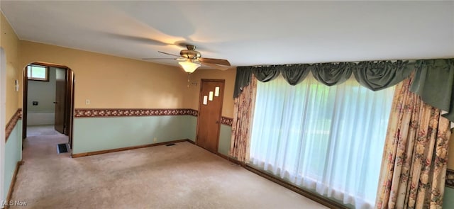 unfurnished room with arched walkways, carpet floors, baseboards, and a ceiling fan