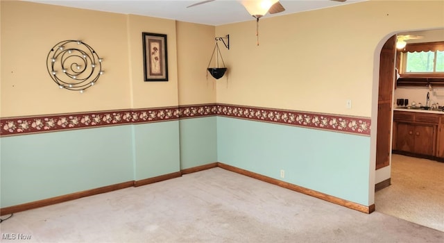 empty room featuring baseboards, ceiling fan, a sink, arched walkways, and carpet floors