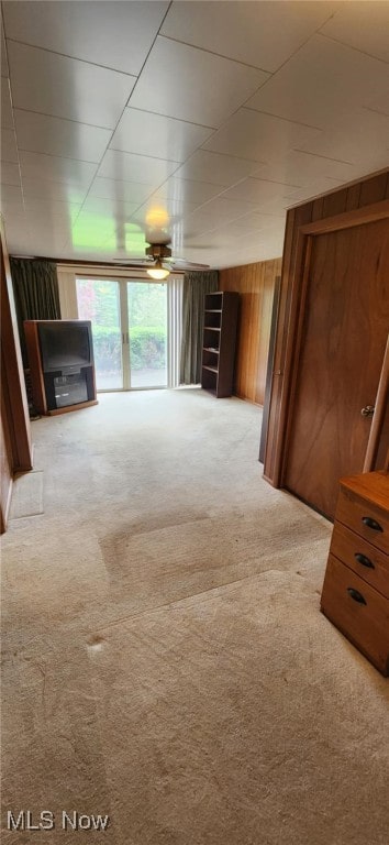 unfurnished living room with ceiling fan, wooden walls, and carpet