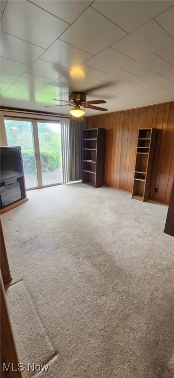 unfurnished living room featuring carpet flooring, wooden walls, and ceiling fan