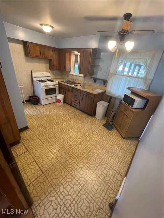 kitchen with white gas range oven, a sink, open shelves, ceiling fan, and light countertops