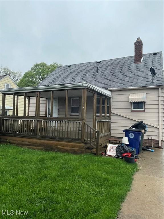 rear view of property featuring a lawn, a chimney, and roof with shingles