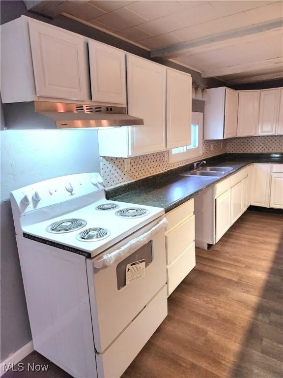 kitchen featuring dark countertops, dark wood-style flooring, under cabinet range hood, white electric range, and decorative backsplash