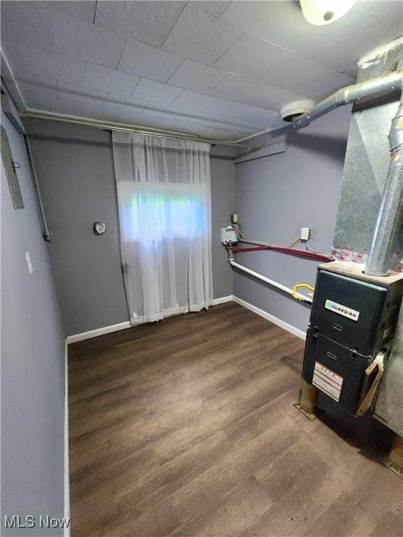 below grade area with baseboards, heating unit, and wood finished floors