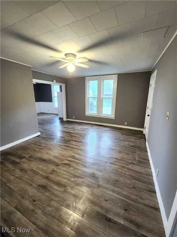 empty room featuring a ceiling fan, baseboards, and dark wood finished floors