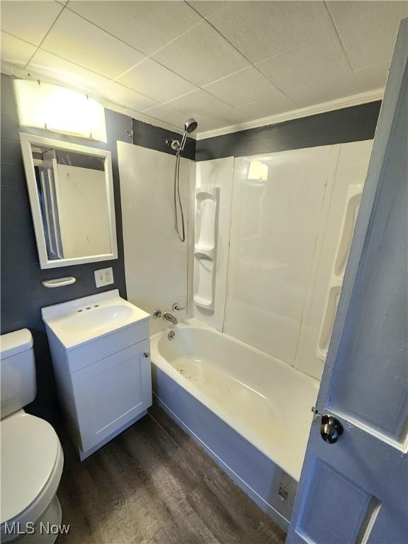 full bath featuring toilet, wood finished floors, vanity, ornamental molding, and bathing tub / shower combination