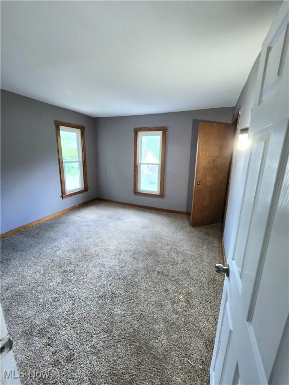 unfurnished bedroom featuring baseboards, multiple windows, and carpet